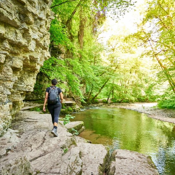 Eine Person mit Rucksack wandert an einem Fluss entlang