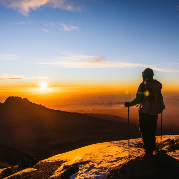 Eine Wanderin blickt vom Gipfel des Kilimandscharo in den Sonnenaufgang