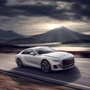 Weißes Auto von Bentley auf einer Straße, im Hintergrund Berge und Wolken