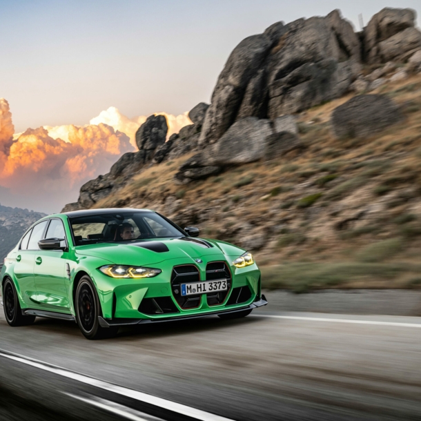 Ein grüner BMW auf einer Landstraße, im Hintergrund große Wolken und Berge