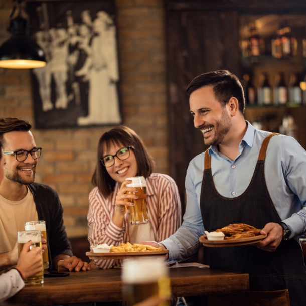 Lächelnder Kellner, der einer Gruppe von Gästen in einem Pub Essen bringt