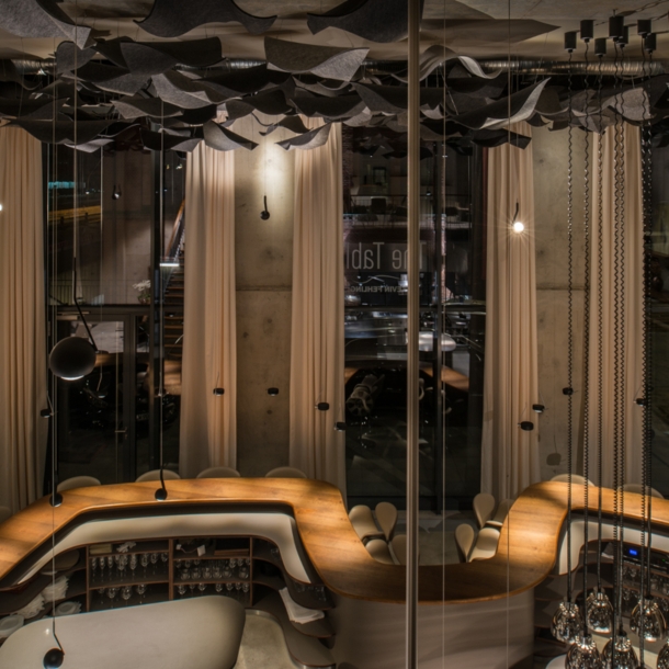 Blick auf das leere Restaurant The Table mit dem geschwungenen Holztisch und hohen Fenstern im Hintergrund