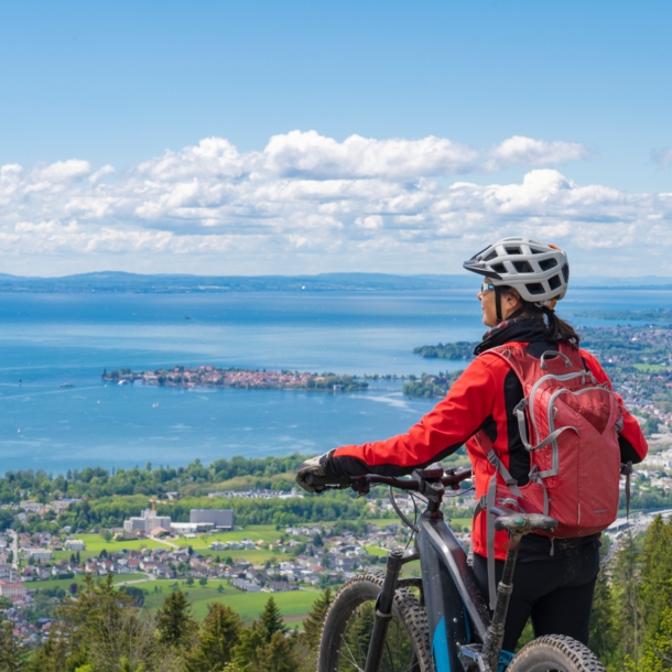 Rückansicht einer Frau mit einem Fahrrad vor dem Panorama des Bodensees