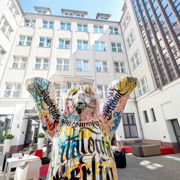 Die Statue eines bunten Berliner Bären steht im Innenhof eines mehrstöckigen weißen Hotels