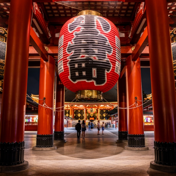 Rote Säulen und überdimensionale Laternen mit japanischen Schriftzügen in einem Tempel