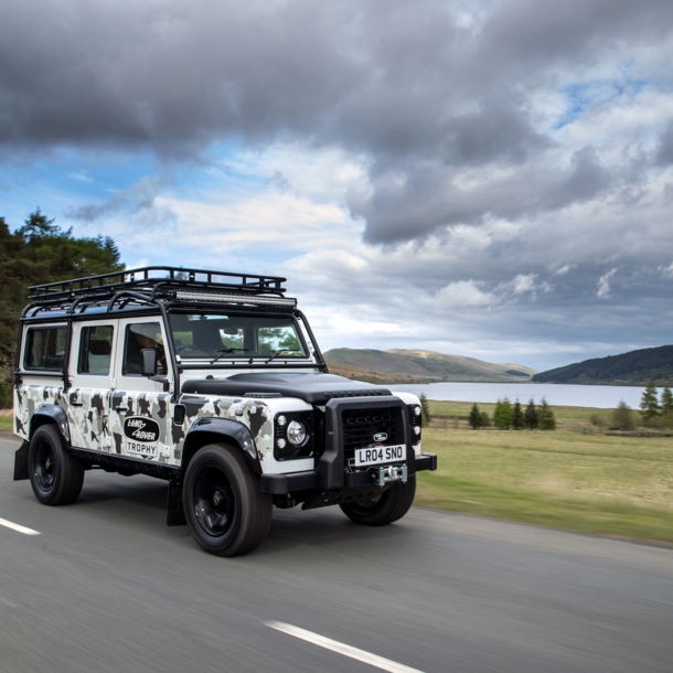 Der Defender Works V8 Trophy II fährt bei bewölktem Wetter an einem See entlang.