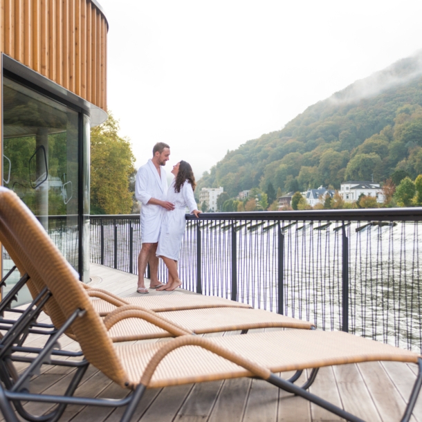 Ein Mann und eine Frau in weißen Bademänteln stehen auf dem Sonnendeck einer Flusssauna