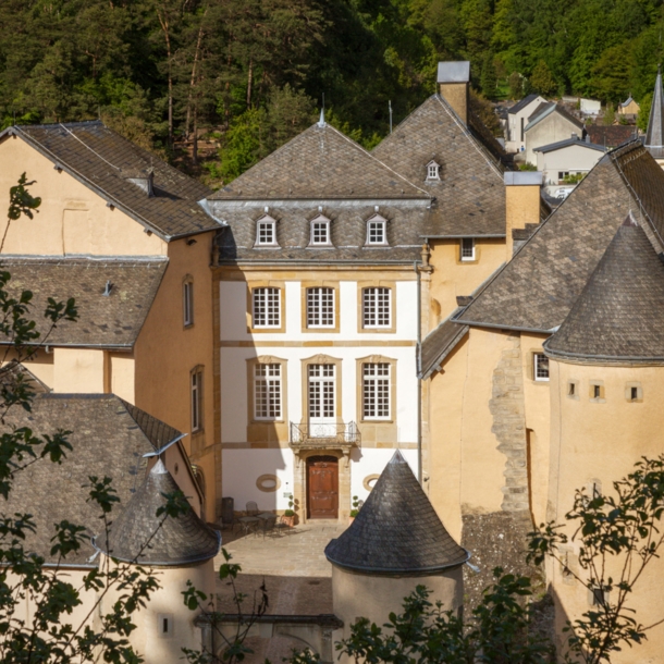 Kleine Burg aus beigem Sandstein mit Rundtürmen und Innenhof in einem bewaldeten Gebiet