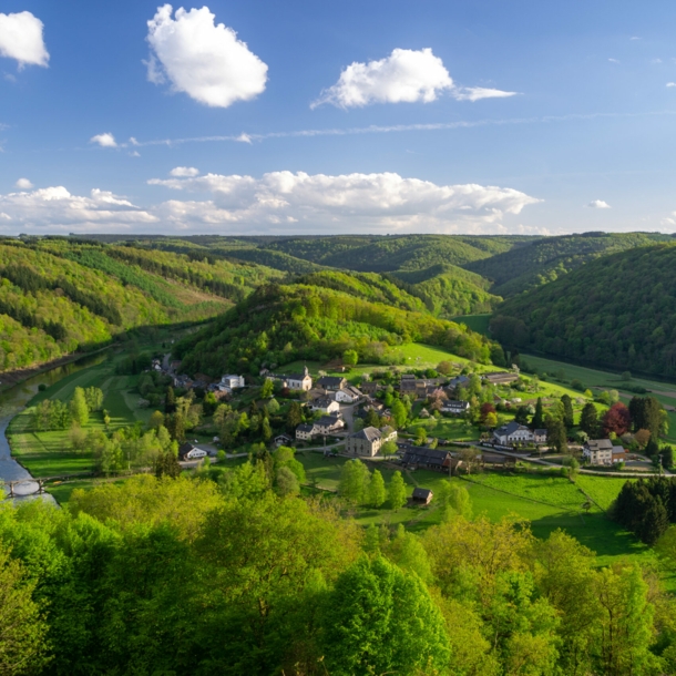 Kleine Ortschaft in einem Flusstal, weitläufig umgeben von hügeliger Waldlandschaft