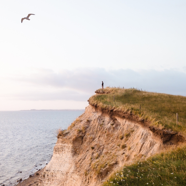 Eine Person steht auf einer Klippe und blickt aufs Meer