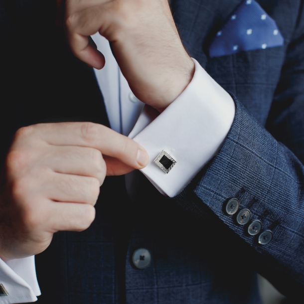 Oberkörper eines Mannes im blauen Anzug mit eleganten Manschettenknöpfen an weißen Hemdmanschetten.