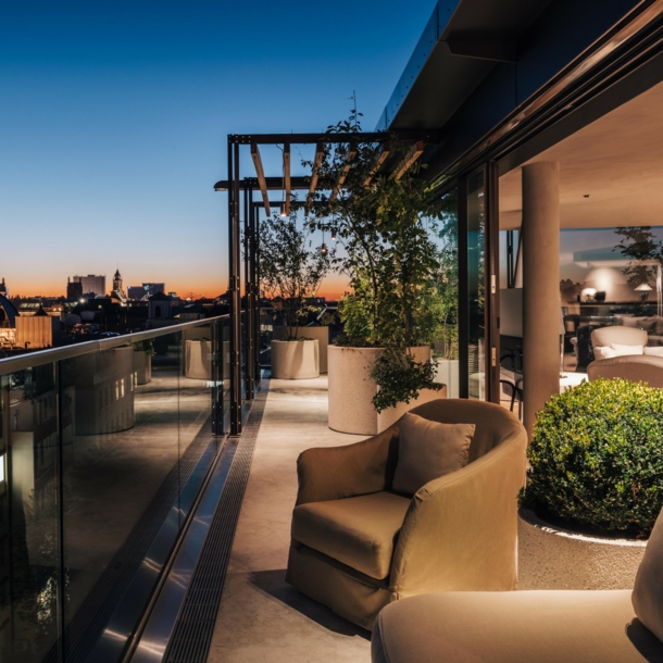 Dachterrasse mit hellen Polstermöbeln vor der Skyline Münchens bei Sonnenuntergang.