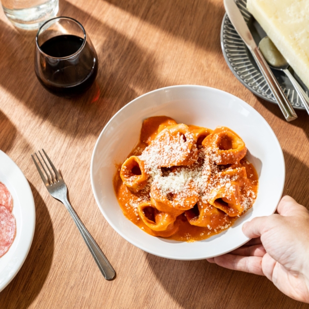 Eine Hand an einem Teller mit Ravioli auf einem eingedeckten Tisch mit Wein und Antipasti