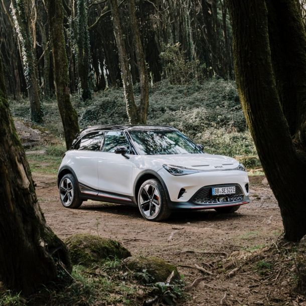 Ein weißer smart #1 BRABUS steht auf einer kleinen Lichtung im Wald. 