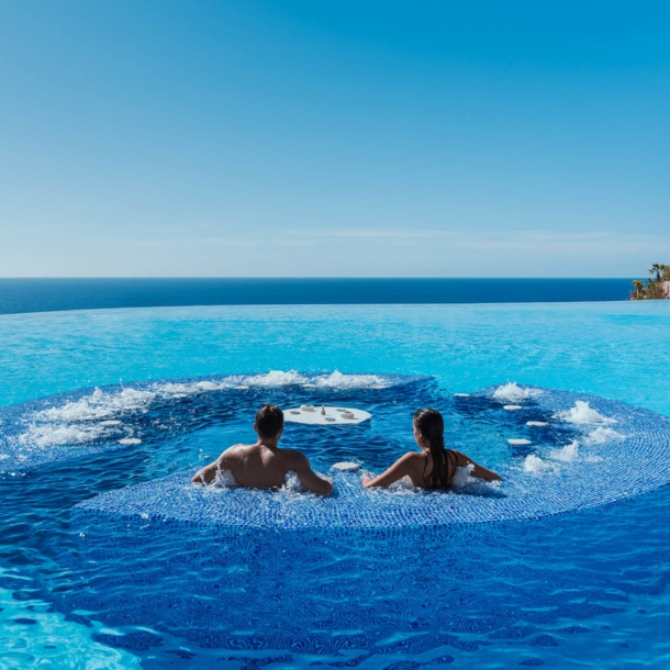 Rückansicht zweier Personen in einem großen Hotelpool mit Jacuzzi am Meer.