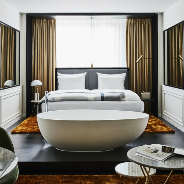 Moderne Hotelsuite mit einer freistehenden Badewanne vor einem Doppelbett.