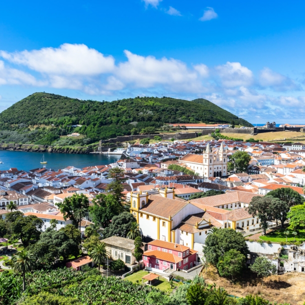 Mediterrane Kleinstadt am Meer, umgeben von grüner Hügellandschaft.