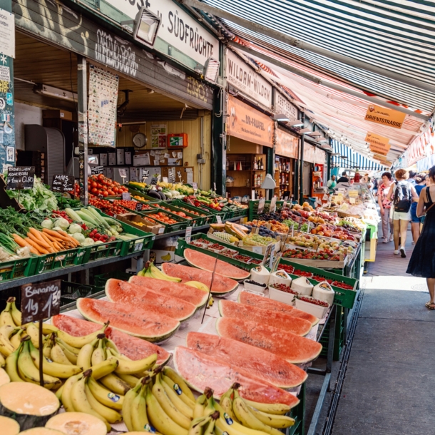 Personen auf einer Marktstraße mit Obst- und Gemüseauslagen.