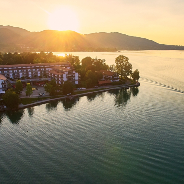 Luxuriöser Hotelkomplex an einem Seeufer, umgeben von Bäumen vor einer bewaldeten Hügellandschaft.