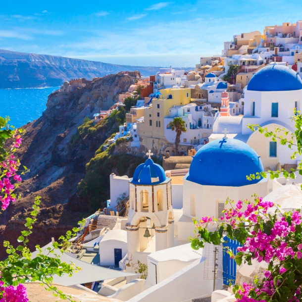 Steilküste von Santorin am Meer mit weißen Häusern mit blauen Dächern, im Vordergrund Bougainvillea.