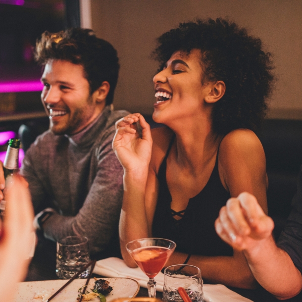 Eine Gruppe junger Menschen sitzt gut gelaunt mit Getränken an einem Tisch in einem Restaurant.