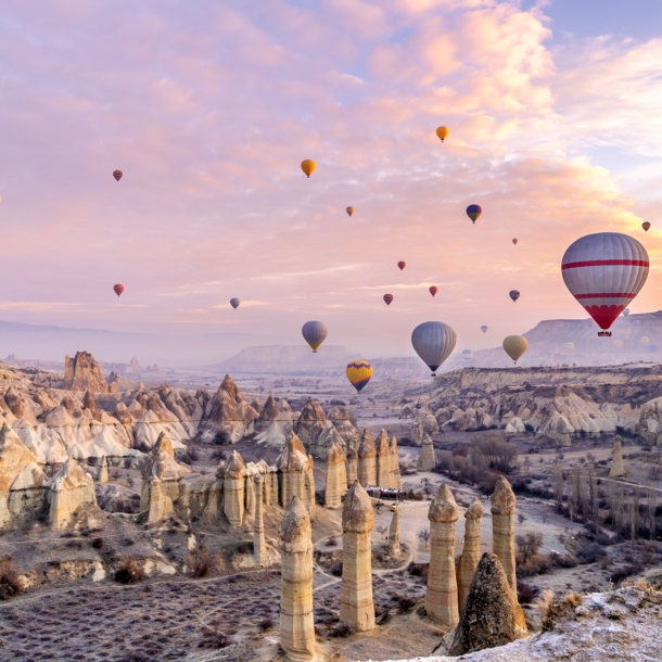 Heißluftballons über einer zerklüfteten Felslandschaft in Kappadokien bei Sonnenuntergang.