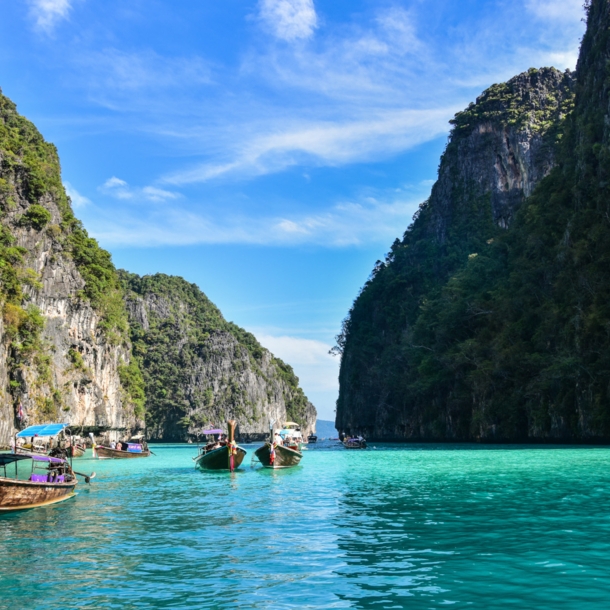 Boote in einer Lagune im türkisblauen Meer mit grün bewachsenen Felsen im Hintergrund. 