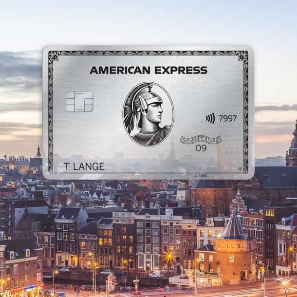 Fotocollage mit Freisteller einer silbernen Kreditkarte von American Express vor dem Stadtpanorama von Amsterdam in der Abenddämmerung.