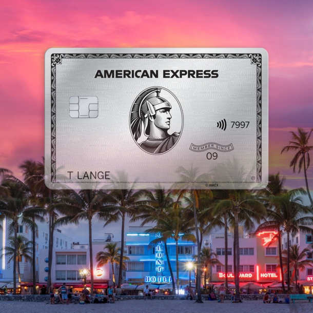 Freisteller einer Platinum Card von American Express vor der erleuchteten Oceanfront von Miami Beach hinter Palmen bei Sonnenuntergang.