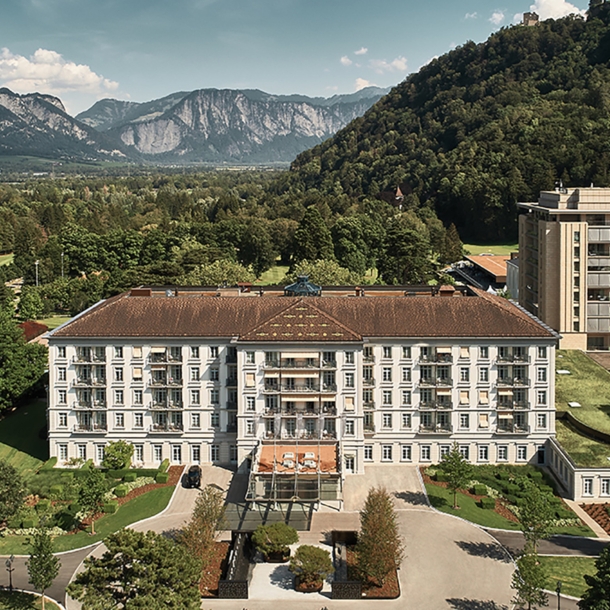 Luftansicht des Grand Resort Bad Ragaz in der Schweiz umgeben von grüner und waldiger Landschaft. Im Hintergrund Berge.