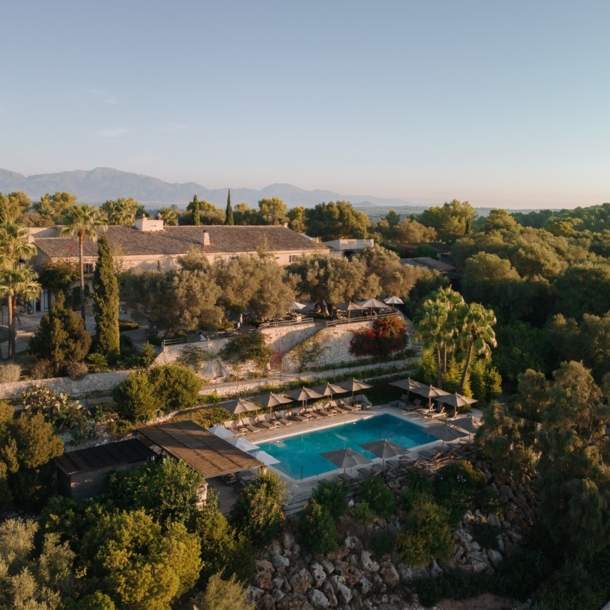 Luftaufnahme einer Finca mit Pool inmitten einer bewaldeten Hügellandschaft.