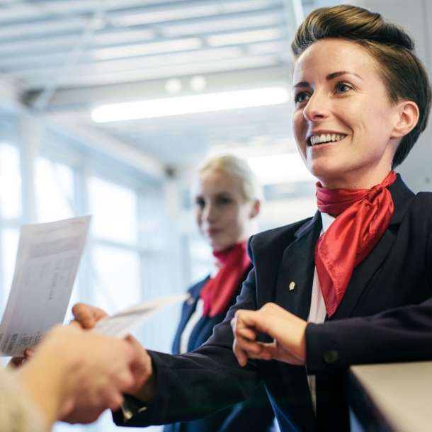 Eine Flugbegleiterin checkt Boardingpässe und begrüßt Reisende am Gate.