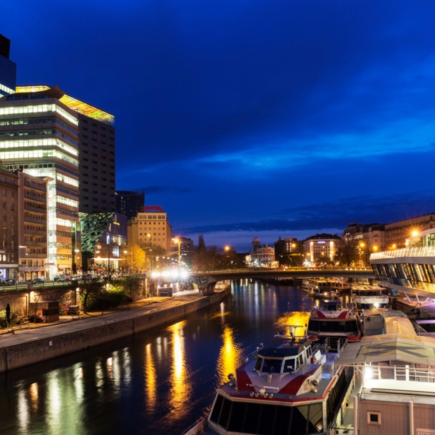 Moderner Hotelkomplex am Donaukanal mit Barkassen in Wien bei Nacht.