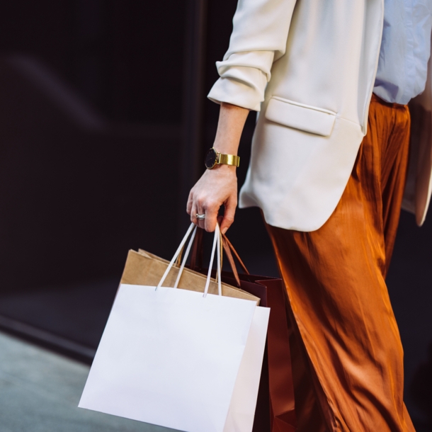 Eine angeschnittene weibliche Person in eleganter Kleidung mit Einkaufstüten in der Hand.