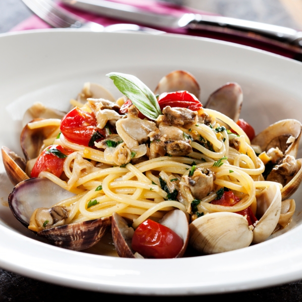 Nahaufnahme einer Portion Spaghetti mit Muscheln und Kirschtomaten auf einem weißen Pastateller.