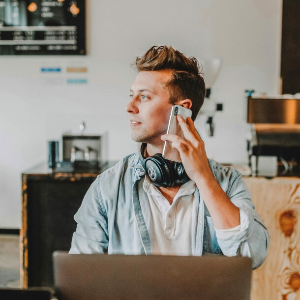 Junger Mann arbeitet im Café am Laptop und telefoniert