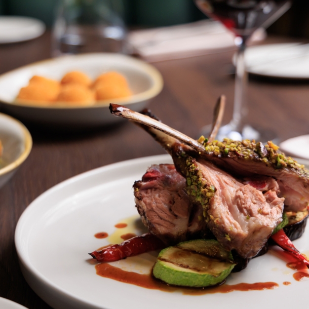 Gegrilltes Lammrippenkotelett, angerichtet auf einem weißen Teller, daneben Beilagen auf einem Tisch in einem Restaurant.