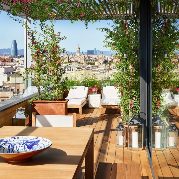 Hotelterrasse mit Liegen vor der Skyline Barcelonas bei Sonnenschein.