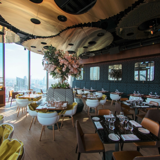 Ein stilvolles Restaurant mit modernen Designelementen und Ausblick auf eine Skyline durch bodentiefe Panoramafenster.