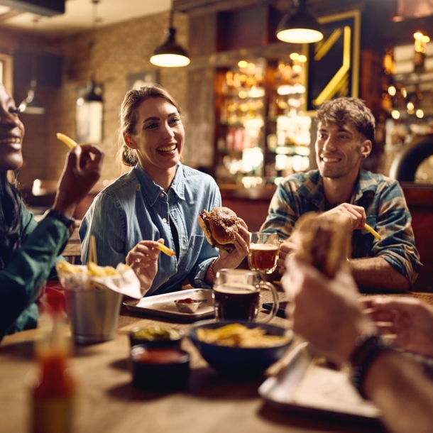 Vier junge Menschen an einem Holztisch essen Fastfood in einem rustikalen Restaurant.