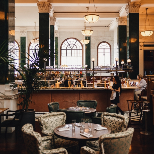 Hotellobby mit grünen Säulen um eine Bar mit Esstischen im 1920er-Jahre-Stil.