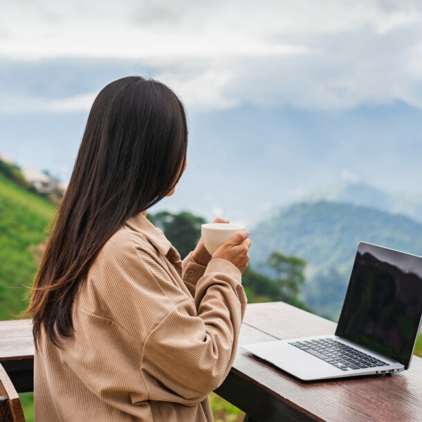 Junge Frau arbeitet auf dem Balkon am Laptop und genießt die Aussicht