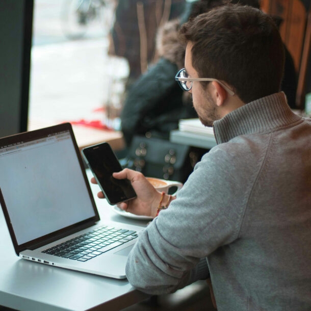 Mann sitzt mit Laptop und im Cafe und schat auf sein Smartphone