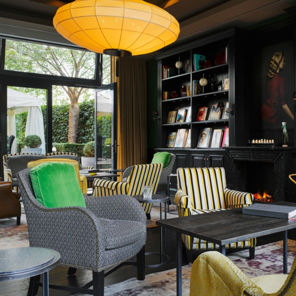 Eine gemütlich eingerichtete Hotellobby mit dunkler Schrankwand, Sesseln in Grau- und Gelbtönen und einer großen Glasfront mit Blick auf die Terrasse