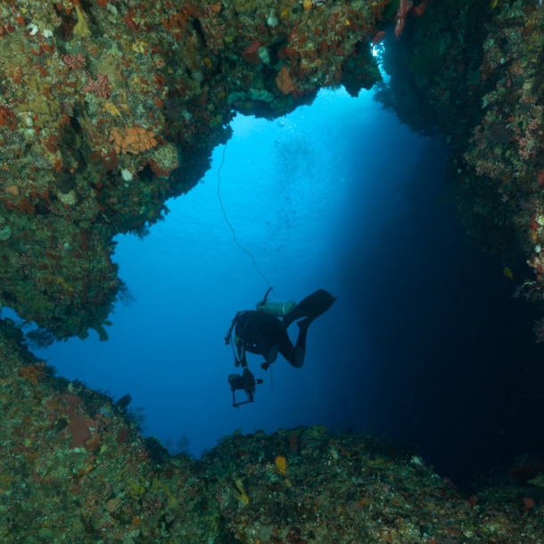 eine Person mit Tauchausrüstung, die aus einer Höhle hinausschwimmt.