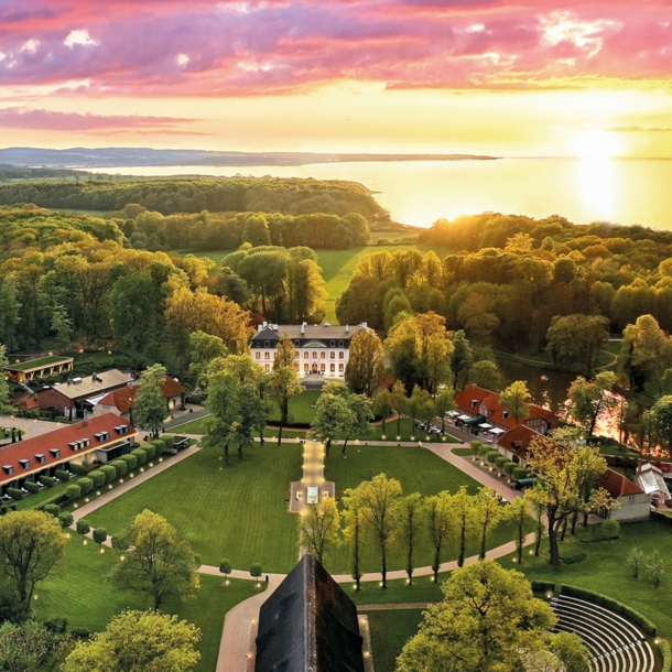 Luxuriöses Hotelresort mit Park- und Waldlandschaft an Meeresküste bei Sonnenuntergang.