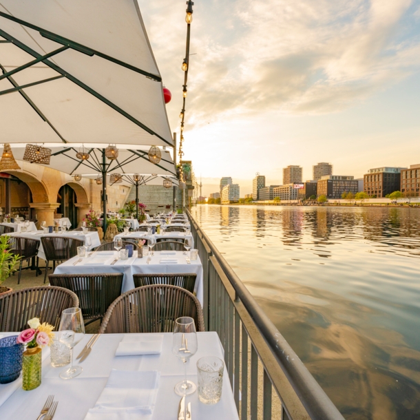 Weiß eingedeckte Tische auf der Terrasse eines eleganten Restaurants am Wasser in Berlin.