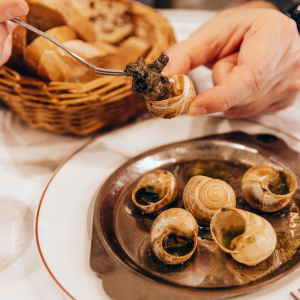 Nahaufnahme von zwei Händen beim Essen von Weinbergschnecken auf einem Teller in einer Brasserie.