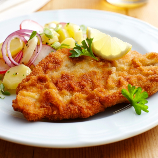 Ein paniertes Schnitzel mit Kartoffelsalat auf einem weißen Teller.