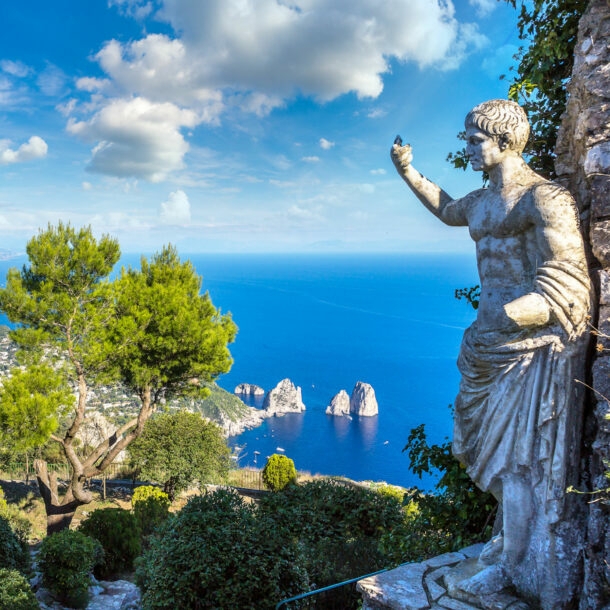 Landschaftspanorama der Insel Capri im blauen Meer, im Vordergrund eine Steinstatue in einem Park.